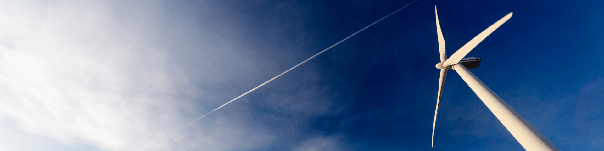 Wind turbine with a trail of a plane overhead and clouds