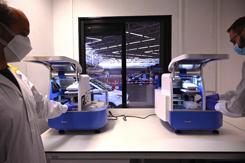 Twee medische specialisten werken in de teststraat van Amsterdam RAI met twee machines aan de resultaten van de corona sneltest die is gebaseerd op de LAMP methode.