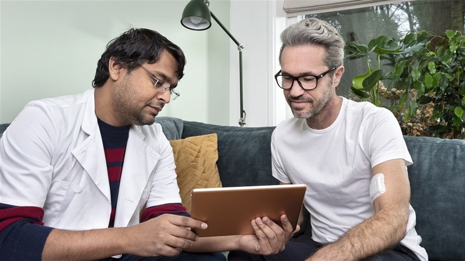 Een patient en zijn dokter bespreken de resultaten van de draagbare medische fotonische patch vanaf een tablet.