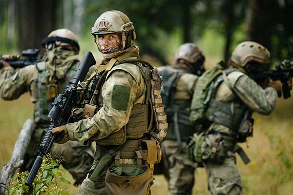 Militairen in camouflagepakken lopen met geweren door het bos