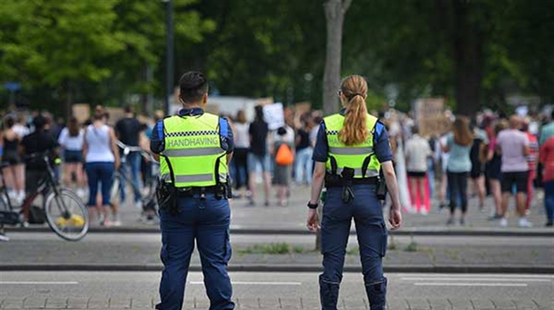 Twee politie mensen kijken naar een groep mensen op straat